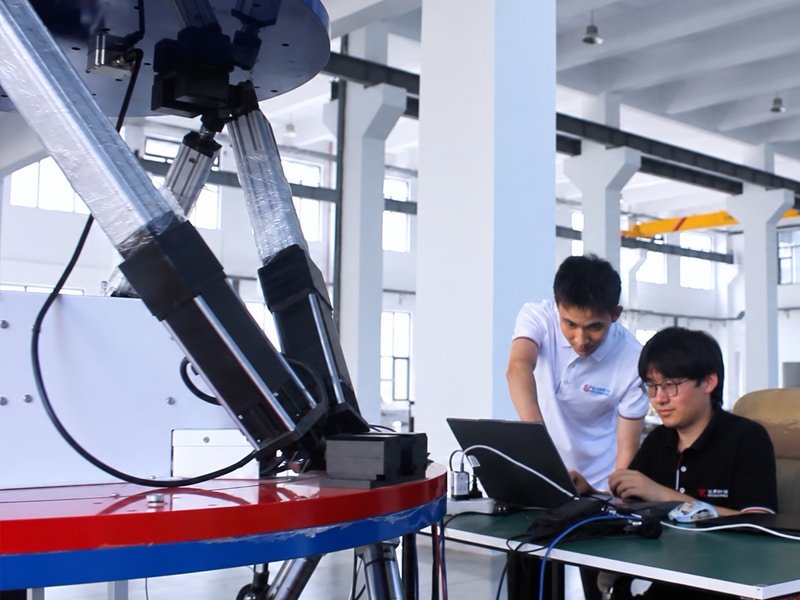 Engineers working at a laptop beside a 6DOF motion platform